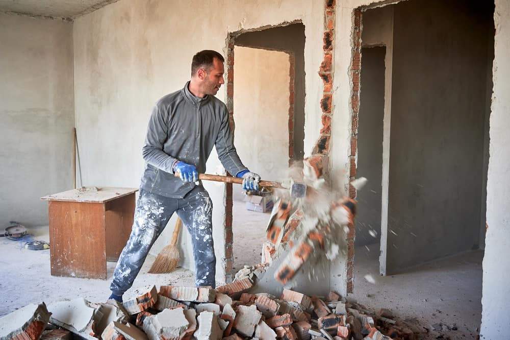Worker removing an interior brick wall during demolition